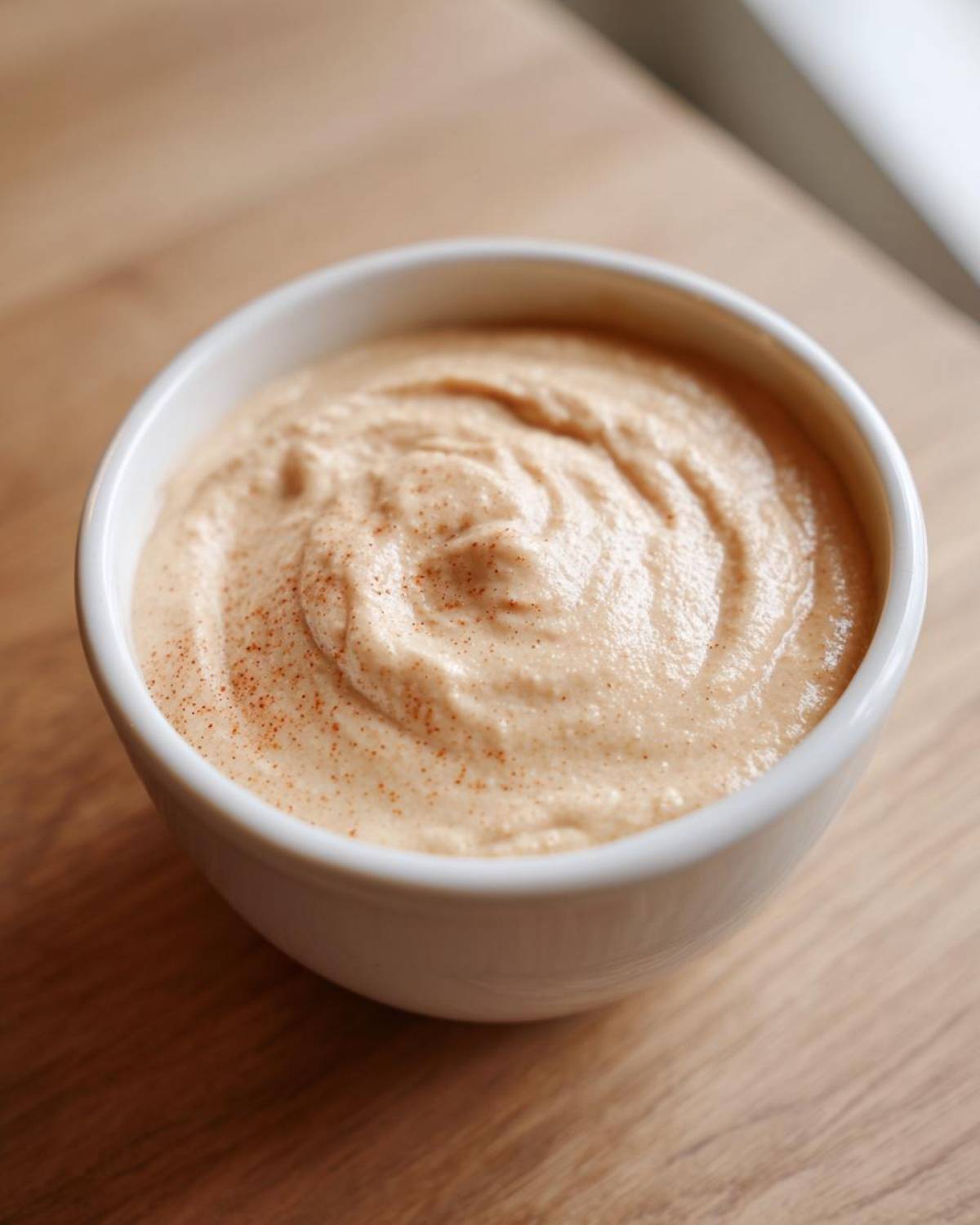 Close-up of thick, creamy cauliflower soup in a white bowl, dusted with paprika or nutmeg.