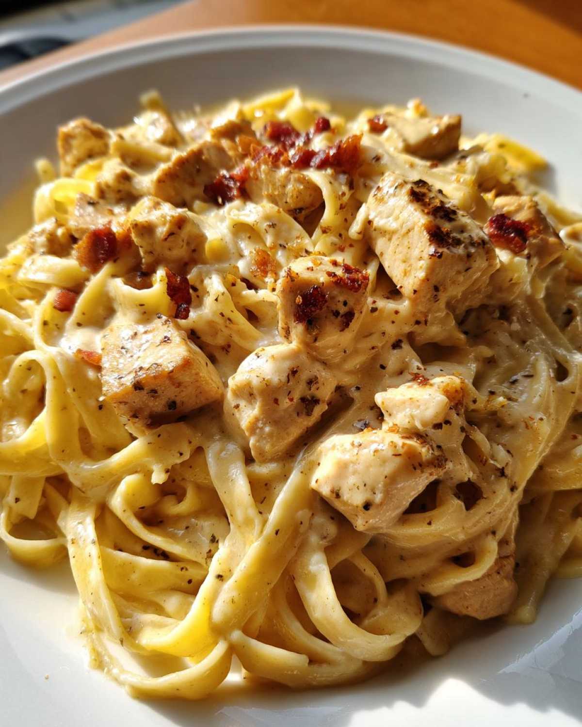 Close-up of rich chicken alfredo pasta featuring fettuccine noodles, seasoned chicken chunks, and crispy bacon bits.