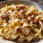 Close-up of creamy fettuccine pasta generously coated in sauce, topped with grilled chicken pieces for chicken alfredo.