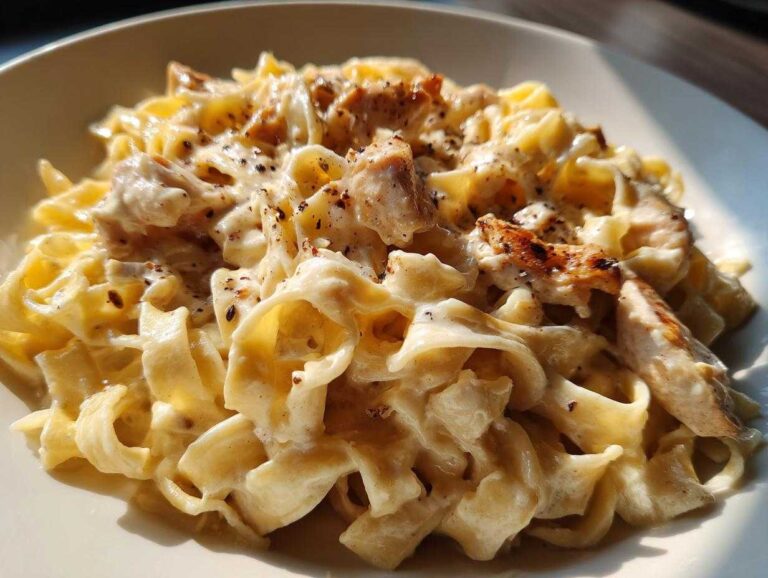 Close-up of creamy fettuccine pasta generously coated in sauce, topped with grilled chicken pieces for chicken alfredo.