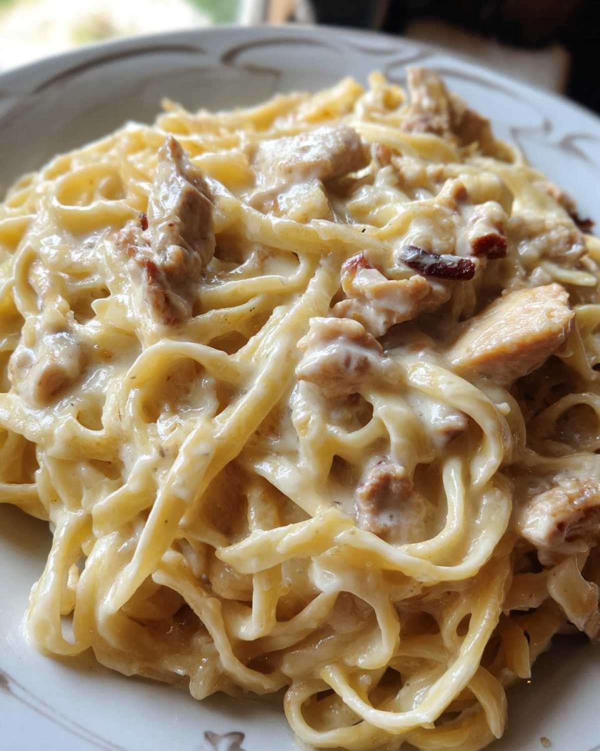 Close-up of fettuccine noodles coated in rich, creamy sauce with chunks of chicken, ready to eat chicken alfredo.