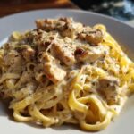 Close-up of creamy chicken alfredo pasta tossed with fettuccine, topped with herbs and parmesan cheese.