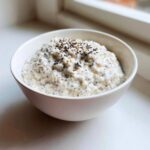 A close-up of creamy coconut chia pudding topped with mixed seeds in a white bowl.