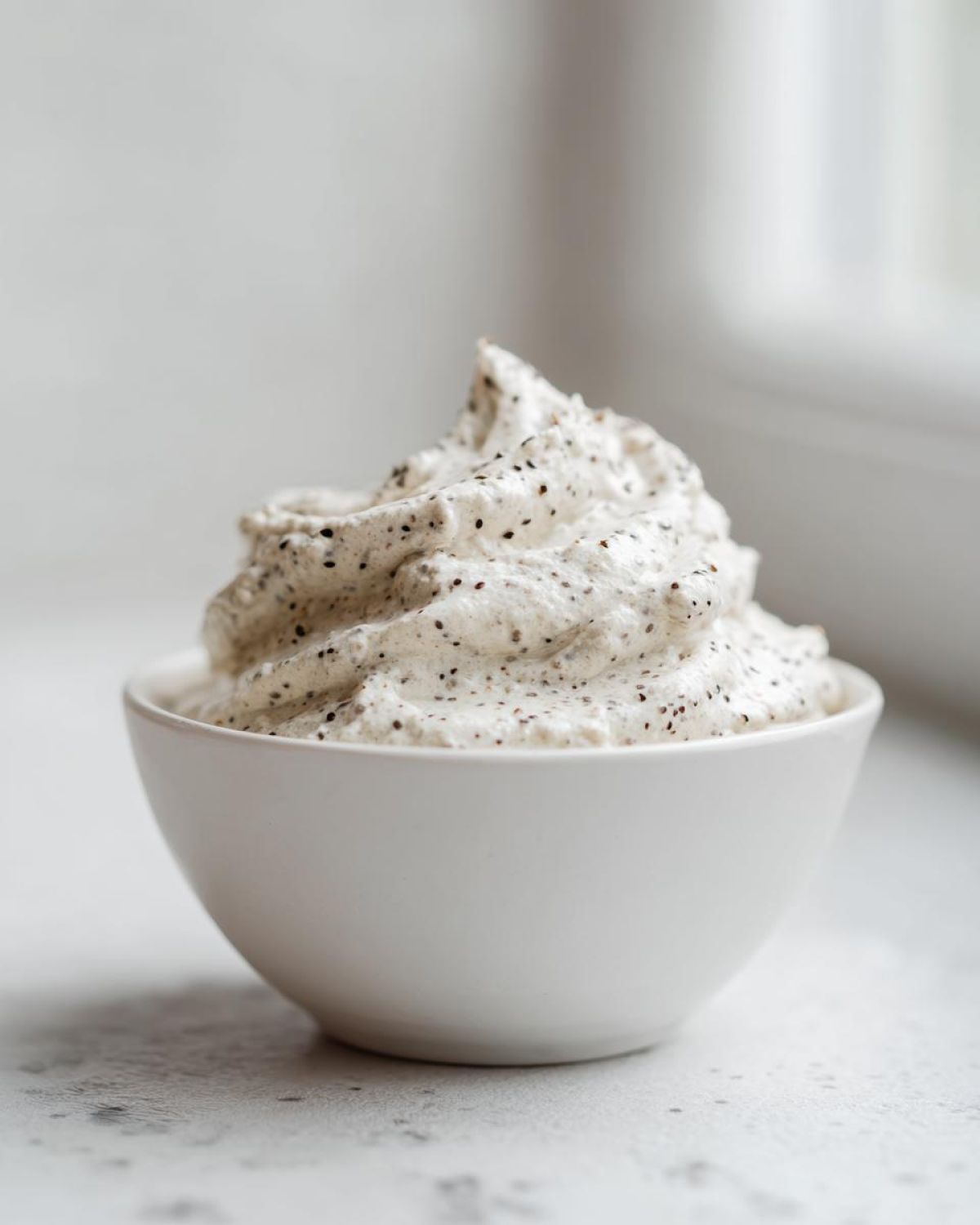 A swirl of creamy coconut chia pudding, speckled with black chia seeds, served in a small white bowl.
