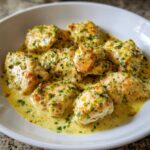 Close-up of seared chicken pieces smothered in a creamy, yellow coconut lime chicken sauce, garnished with green herbs.