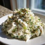 A generous mound of creamy crab salad mixed with celery and herbs, served on a white plate.