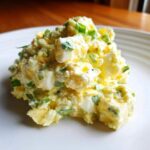 A close-up, appetizing mound of creamy egg salad recipe featuring large chunks of egg white and yolk, topped with fresh green chives.