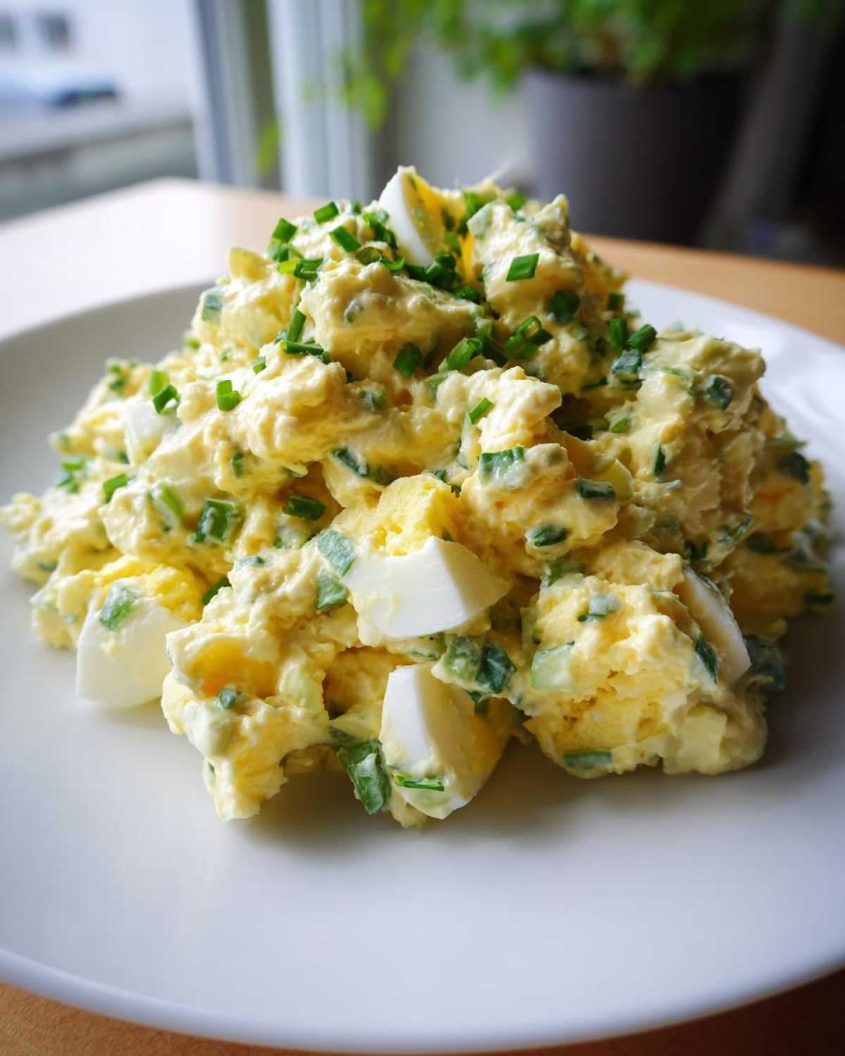A generous mound of creamy egg salad recipe, topped with fresh chopped chives, served on a white plate.