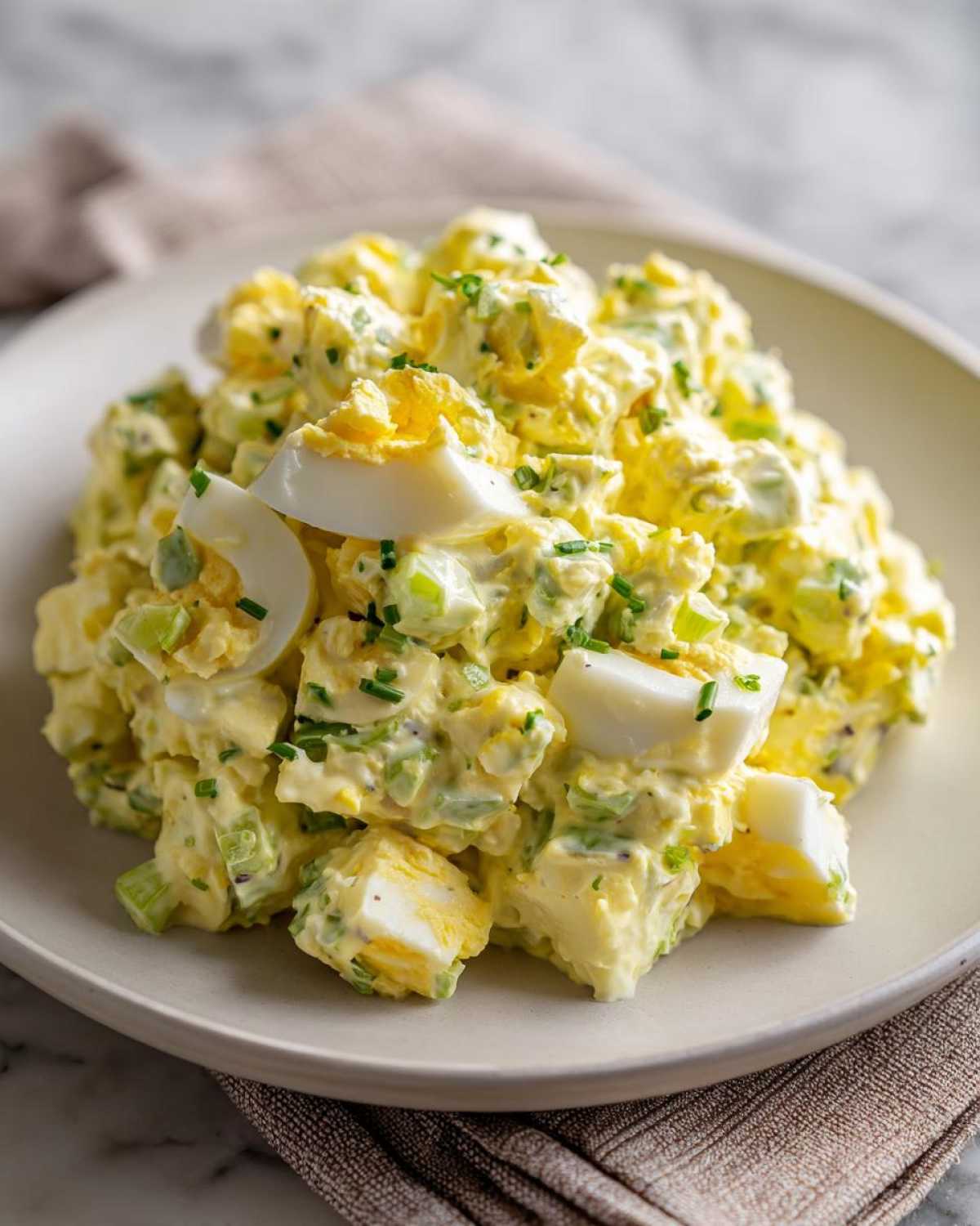 Close-up of a generous serving of creamy egg salad recipe, garnished with chopped chives and visible chunks of hard-boiled egg.