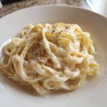 Close-up of fettuccine pasta coated in rich homemade alfredo sauce, topped with grated cheese and black pepper.