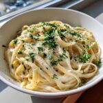 Close-up of creamy garlic parmesan pasta tossed in a white bowl, topped with fresh parsley and grated cheese.