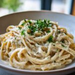 Close-up of creamy pasta coated in sauce, topped with grated cheese and fresh parsley, highlighting the garlic parmesan flavor.