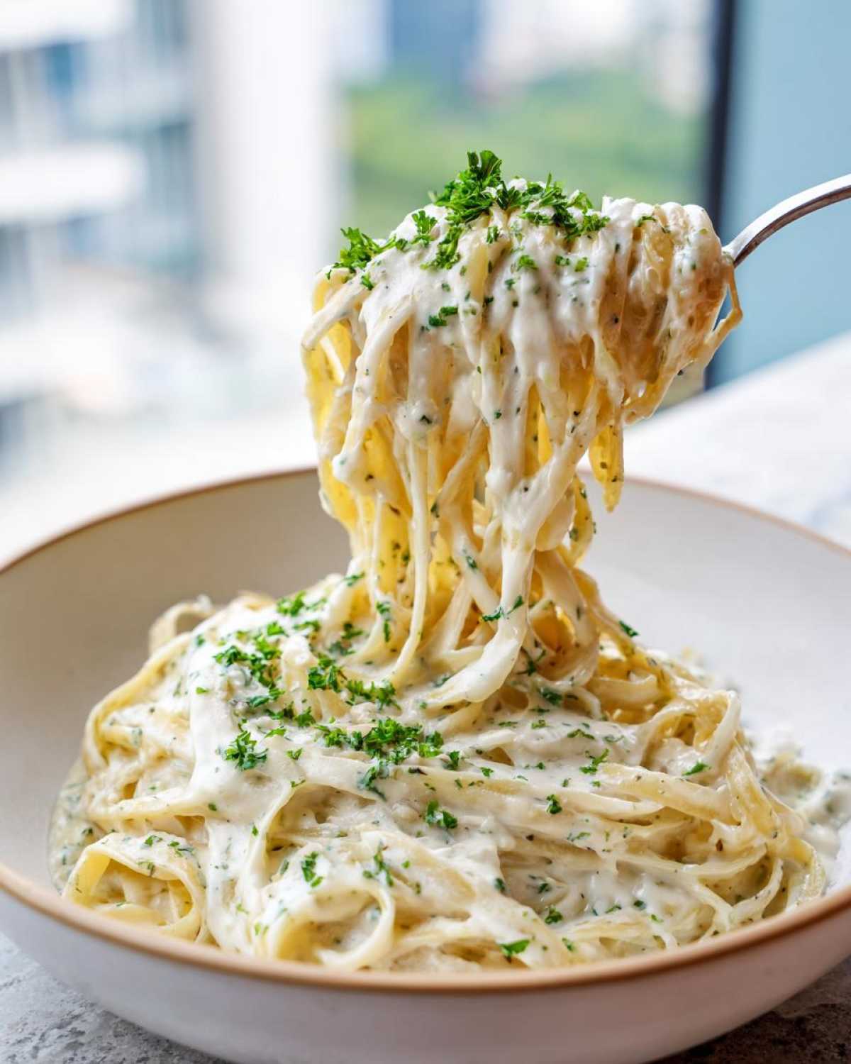 A fork lifting a generous portion of creamy garlic parmesan pasta coated in white sauce and topped with parsley.
