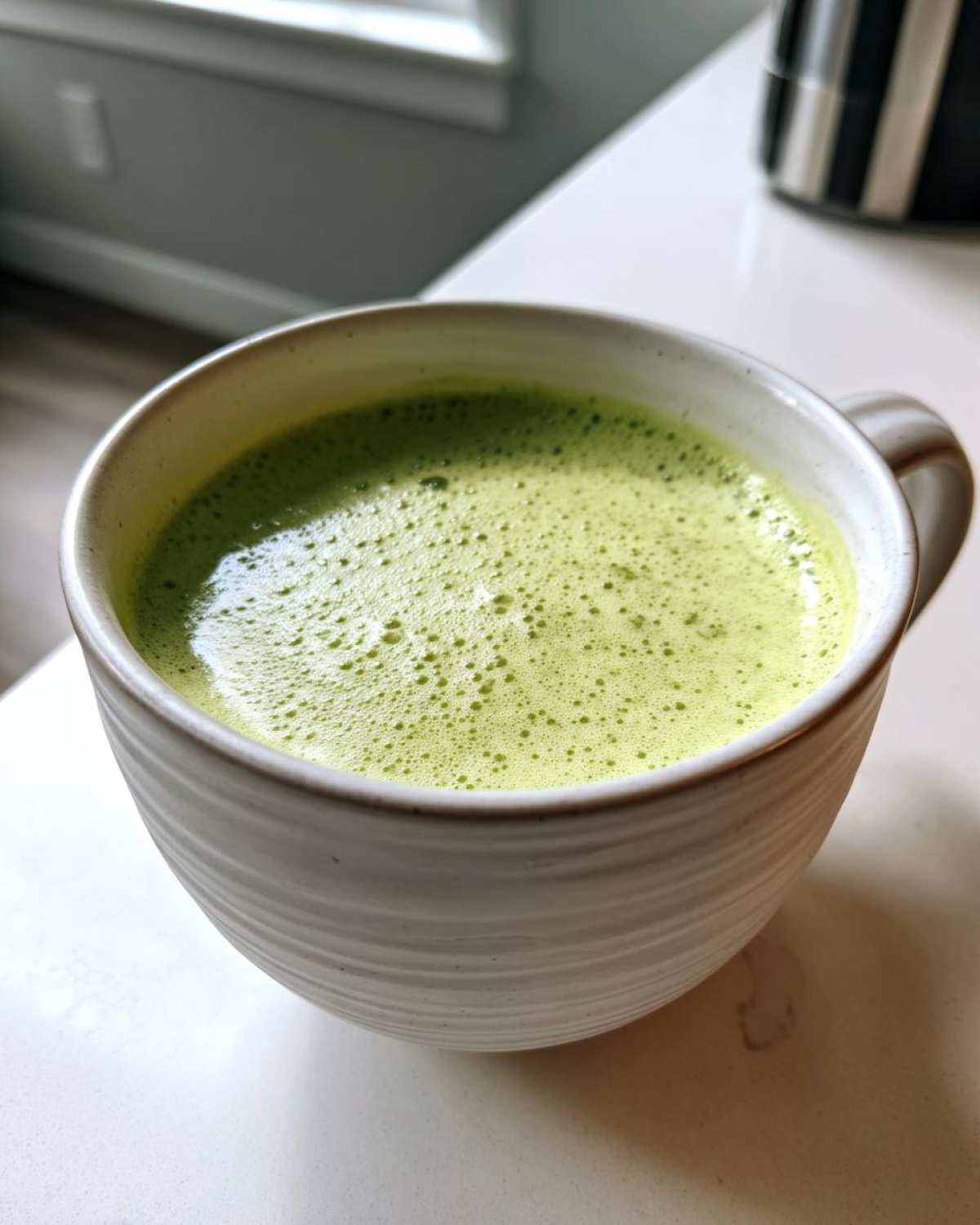 Close-up of a creamy, bright green beverage, resembling leek soup, in a textured white mug.