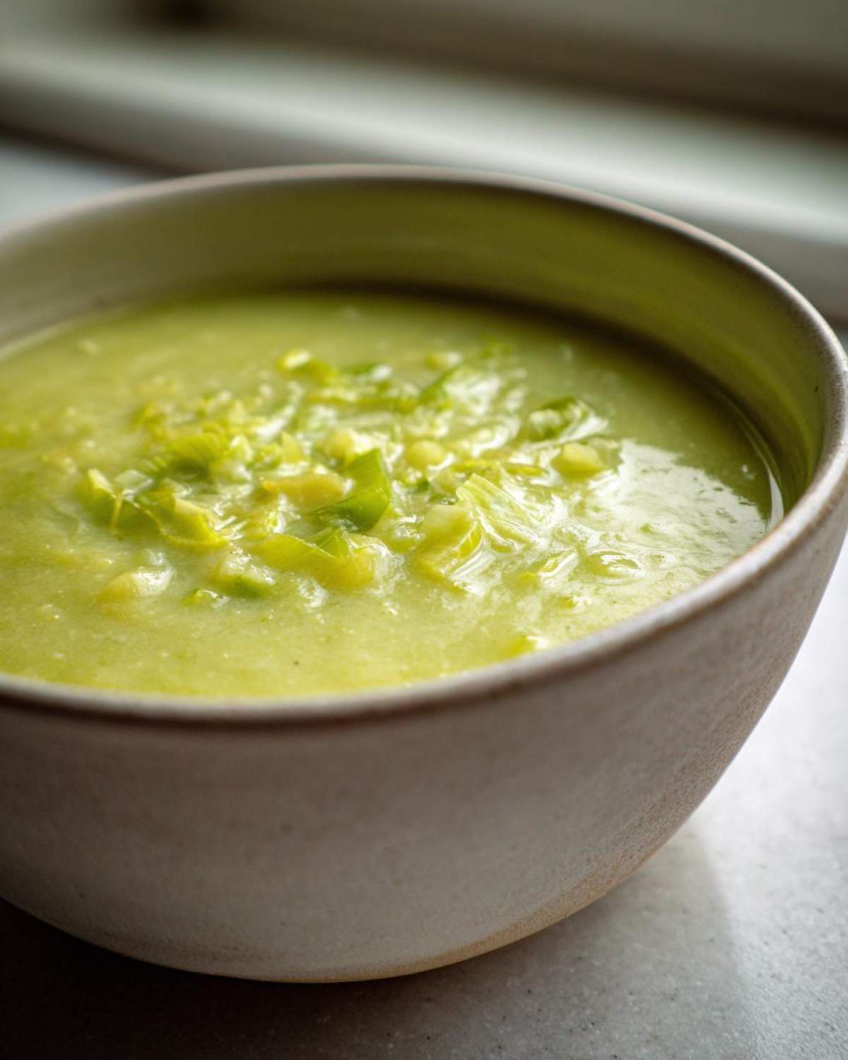 Close-up of creamy, pale green leek soup topped with sautéed leek pieces in a light-colored rustic bowl.