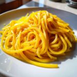 A close-up shot of bright yellow creamy lemon pasta tossed with black pepper, served on a white plate.