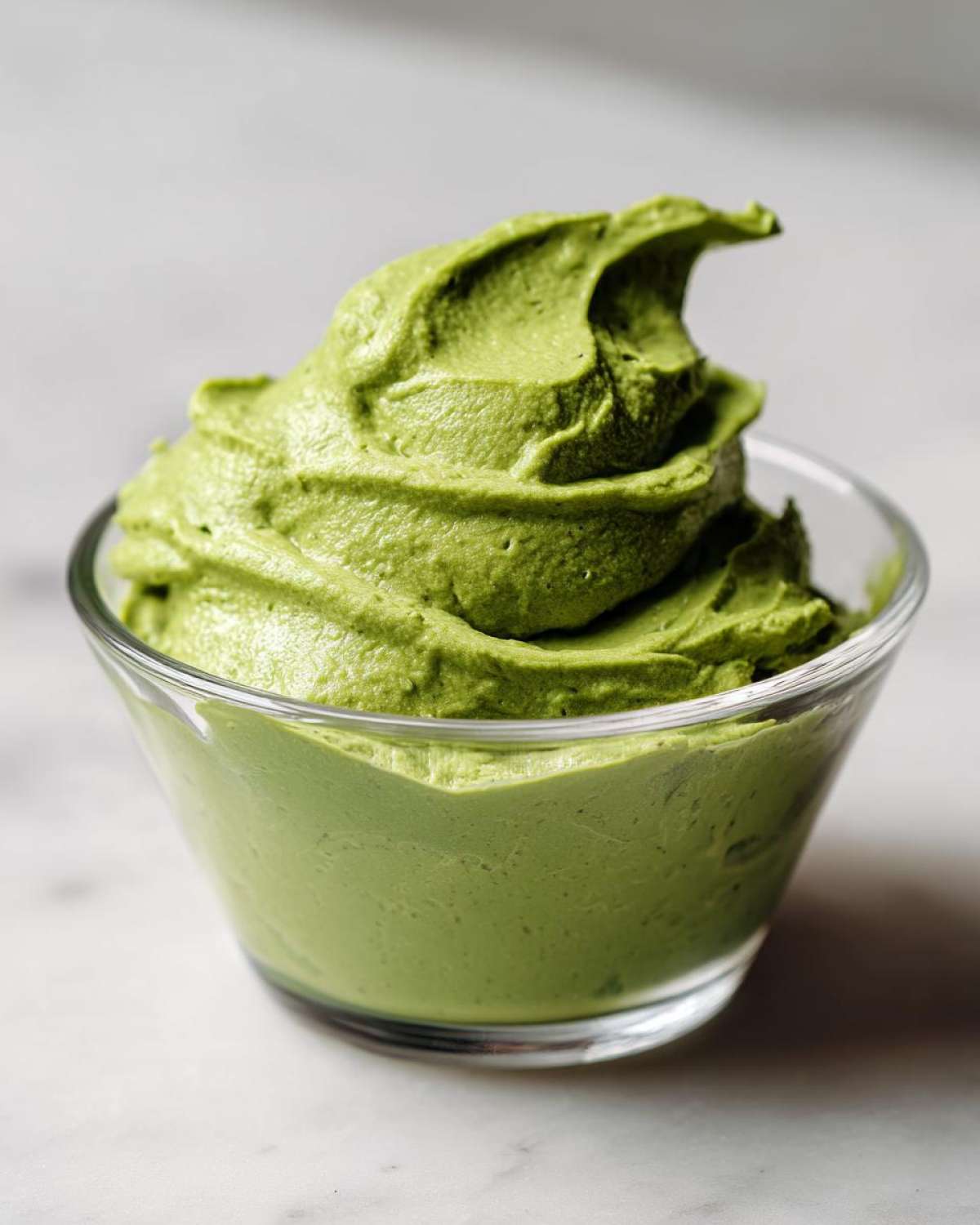 A close-up of thick, vibrant green matcha chia pudding swirled high in a small glass bowl.