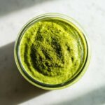 Overhead view of creamy matcha chia pudding in a glass jar, topped with a mound of vibrant green matcha powder.
