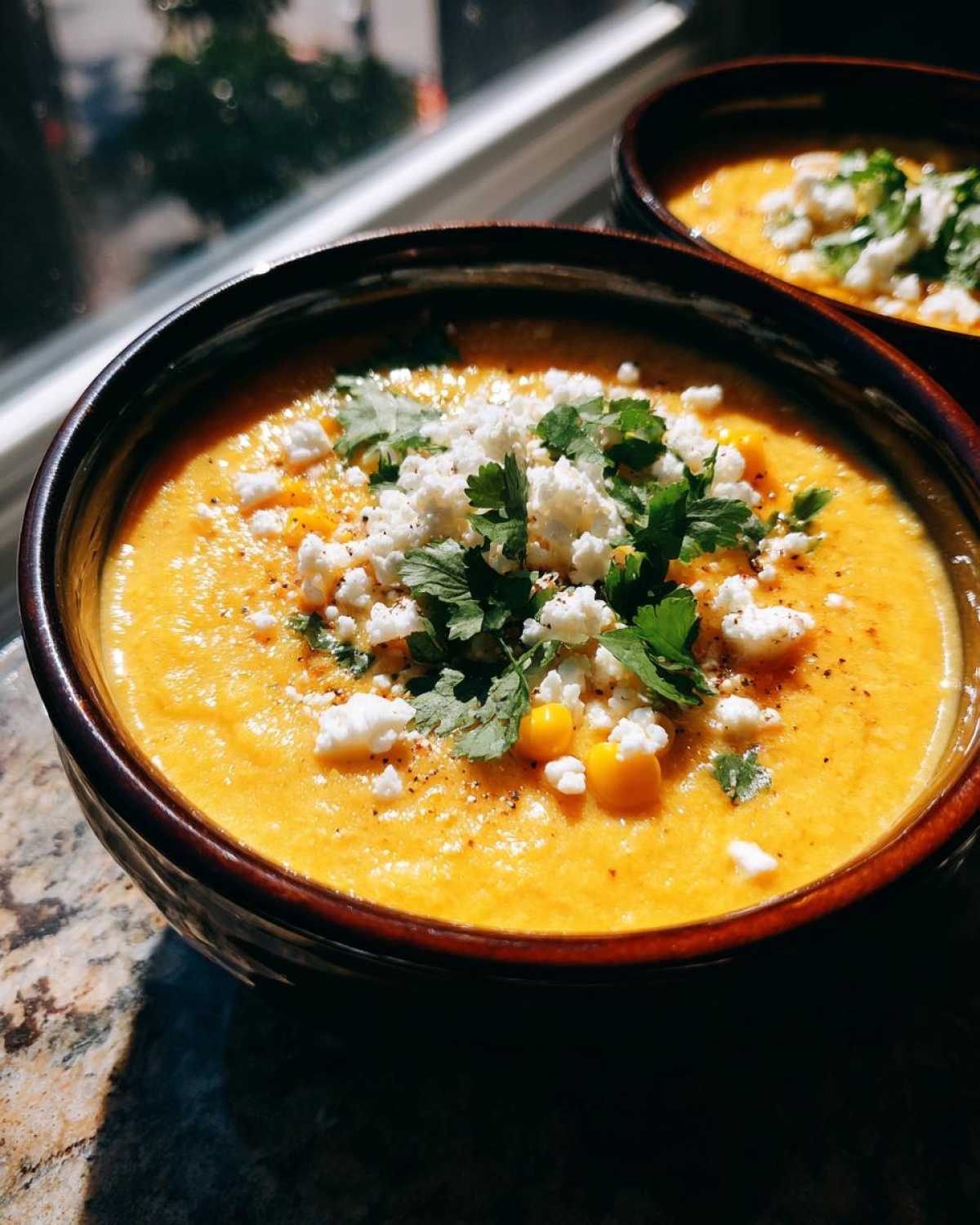 Close-up of a bowl of vibrant orange mexican street corn soup topped with crumbled cheese and cilantro.