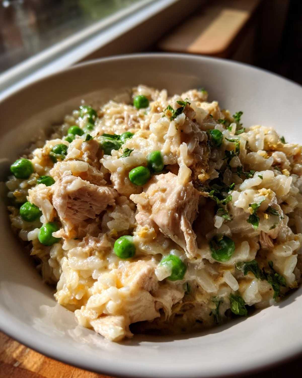 Close-up of a creamy bowl of one pot chicken and rice mixed with bright green peas and fresh parsley.
