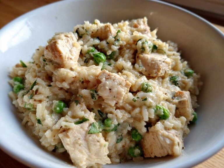 Close-up of creamy one pot chicken and rice mixed with bright green peas and herbs in a white bowl.