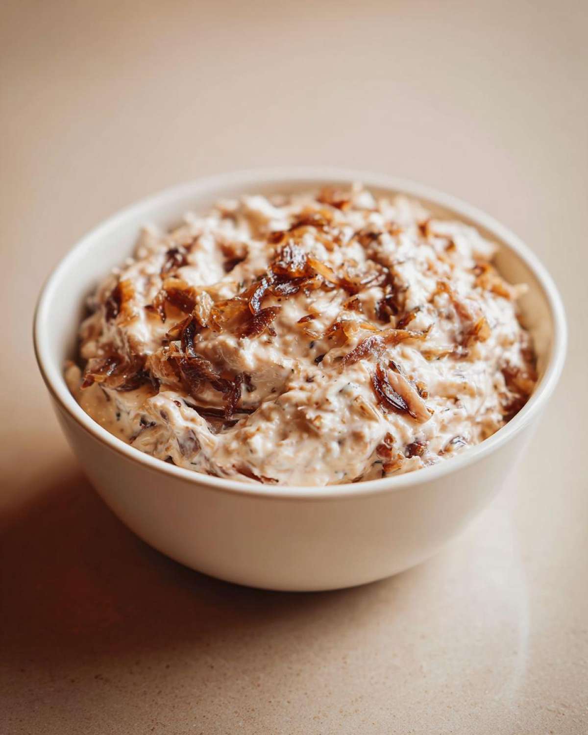 A white bowl filled with creamy onion dip topped generously with crispy, caramelized onions.