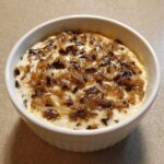 Close-up of a creamy, white onion dip generously topped with dark, caramelized onions in a white bowl.