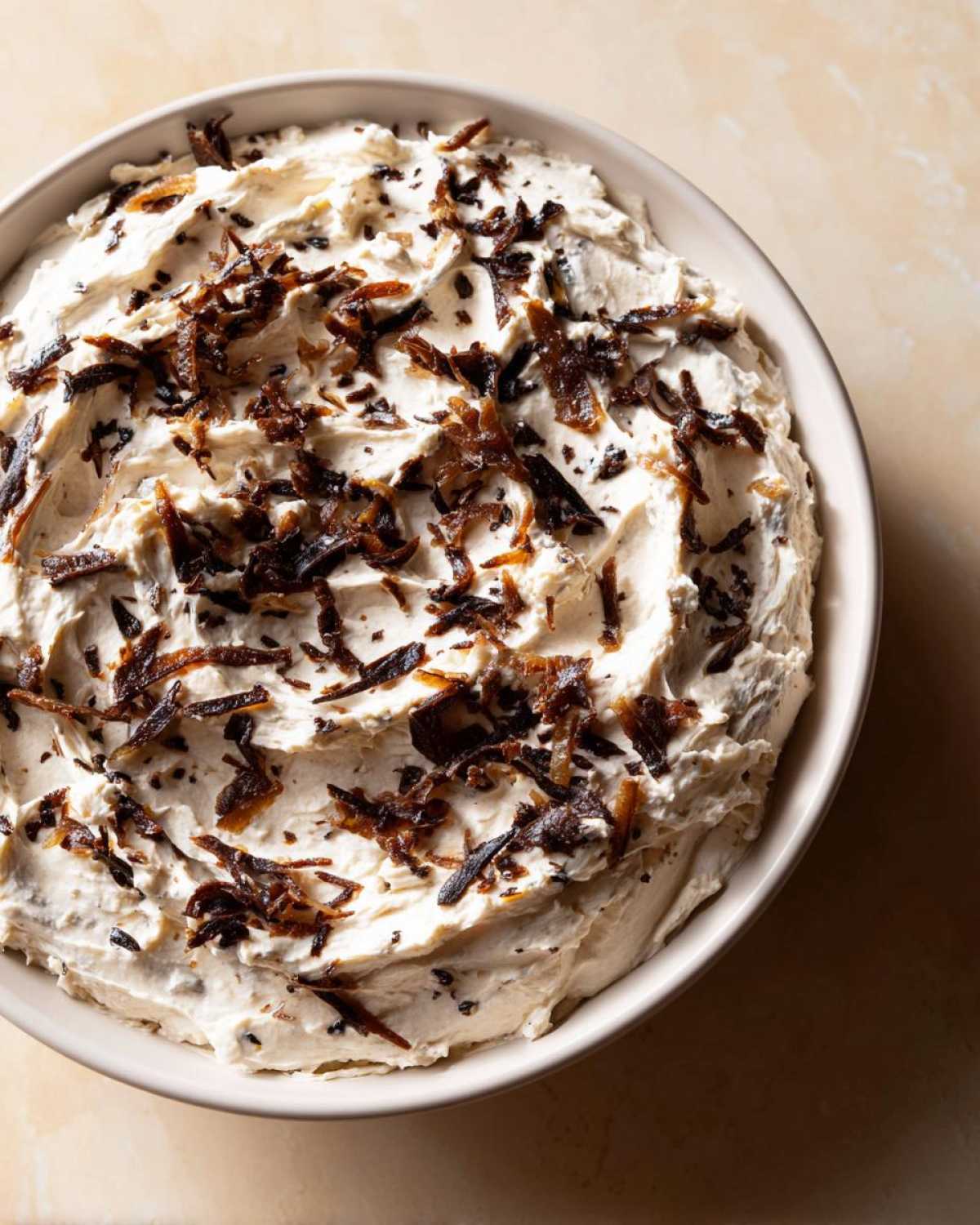 Overhead view of a creamy onion dip topped generously with dark, caramelized onion pieces.