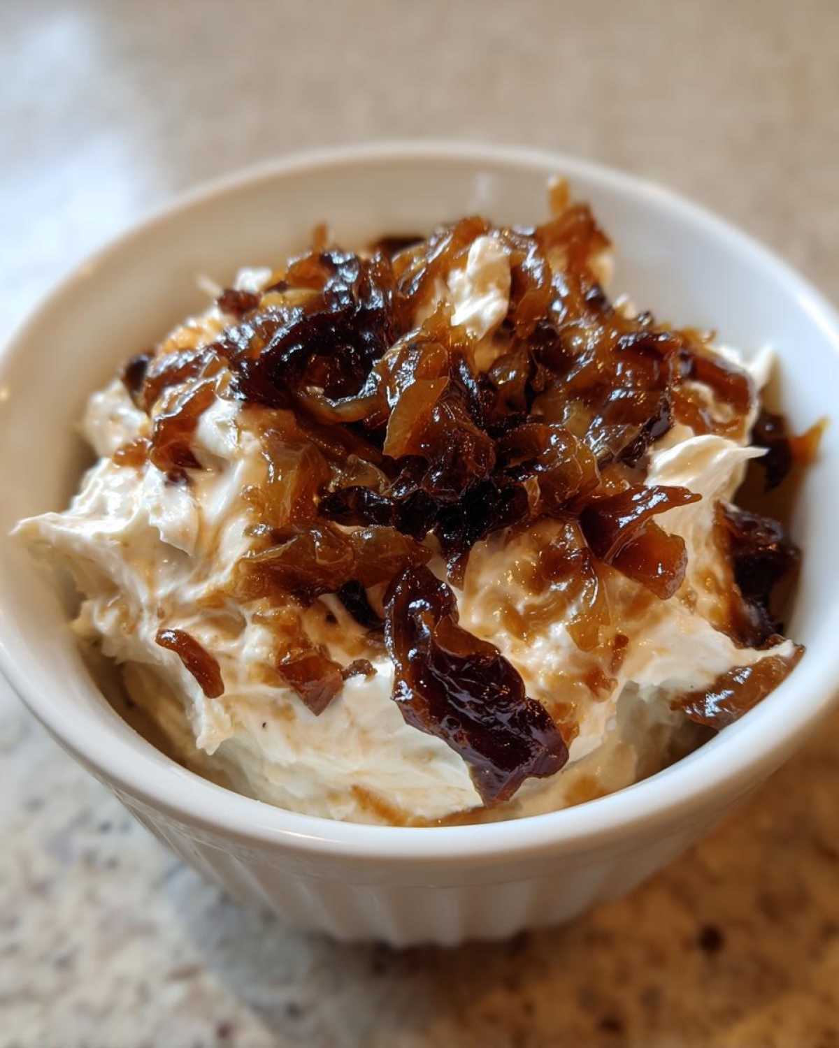 Close-up of creamy onion dip topped generously with dark, caramelized onions in a white bowl.