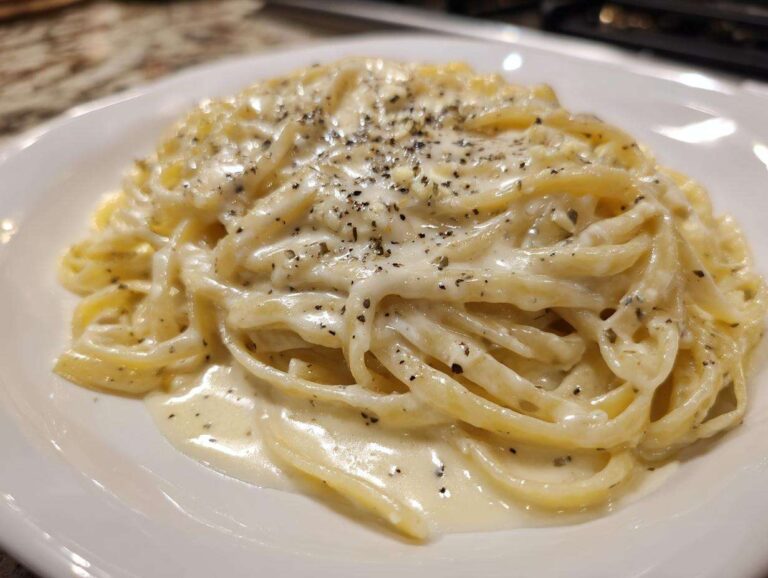 Close-up of fettuccine pasta generously coated in creamy homemade alfredo sauce and topped with cracked black pepper.