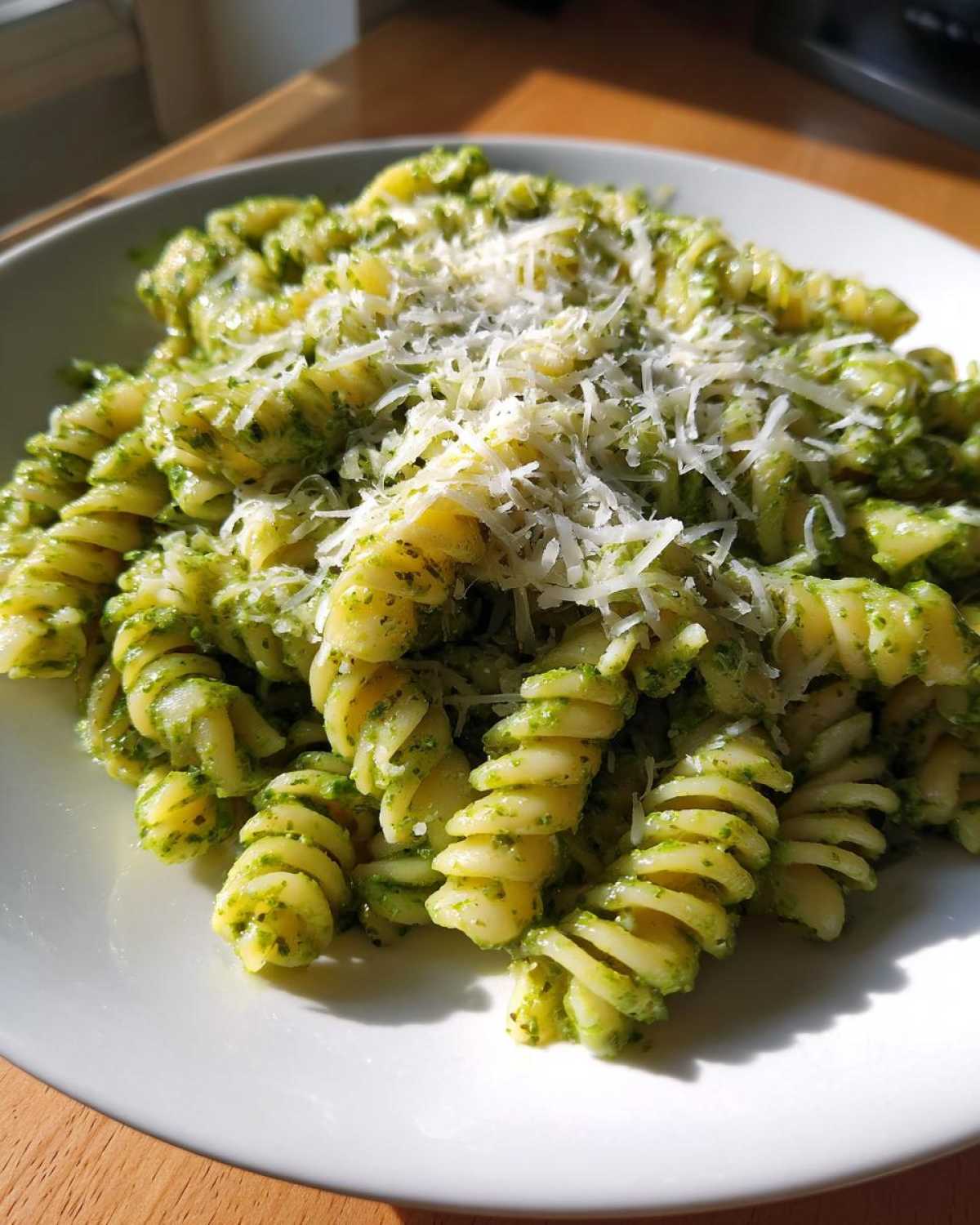 Close-up of creamy pesto pasta using fusilli noodles, topped generously with grated Parmesan cheese.
