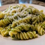 Close-up of creamy pesto pasta made with fusilli noodles, topped generously with shredded Parmesan cheese.