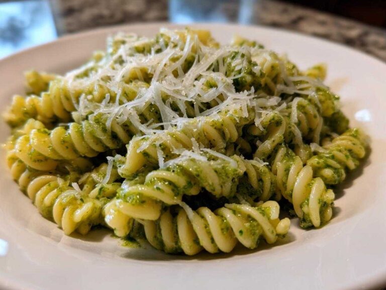 Close-up of creamy pesto pasta made with fusilli noodles, topped generously with shredded Parmesan cheese.