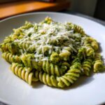 Close-up of creamy pesto pasta made with fusilli, topped generously with shredded Parmesan cheese.
