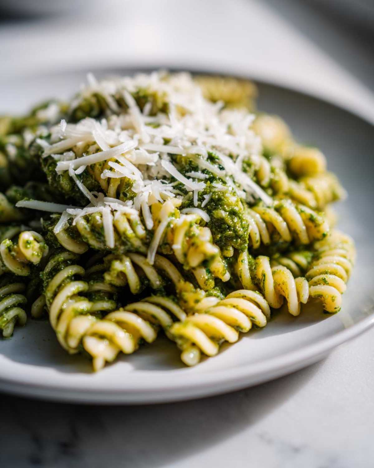 Close-up of creamy pesto pasta made with fusilli, topped generously with grated Parmesan cheese.