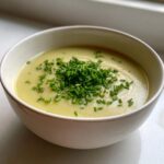 A close-up of creamy potato leek soup in a white bowl, generously topped with fresh green chives.