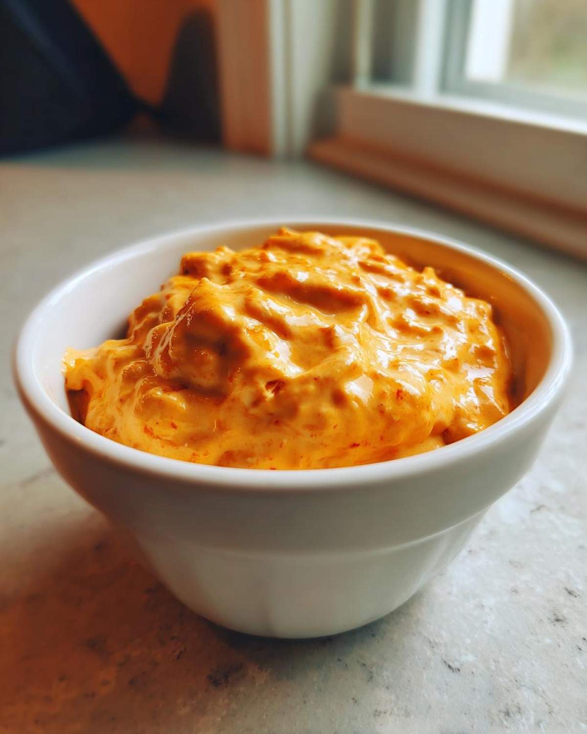Close-up of creamy, orange-colored rotel dip served in a small white bowl on a light countertop.