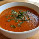 Close-up of a bowl of creamy tomato basil soup garnished with fresh, thinly sliced basil.