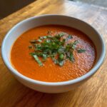 A white bowl filled with creamy tomato basil soup, topped generously with fresh, chopped basil.