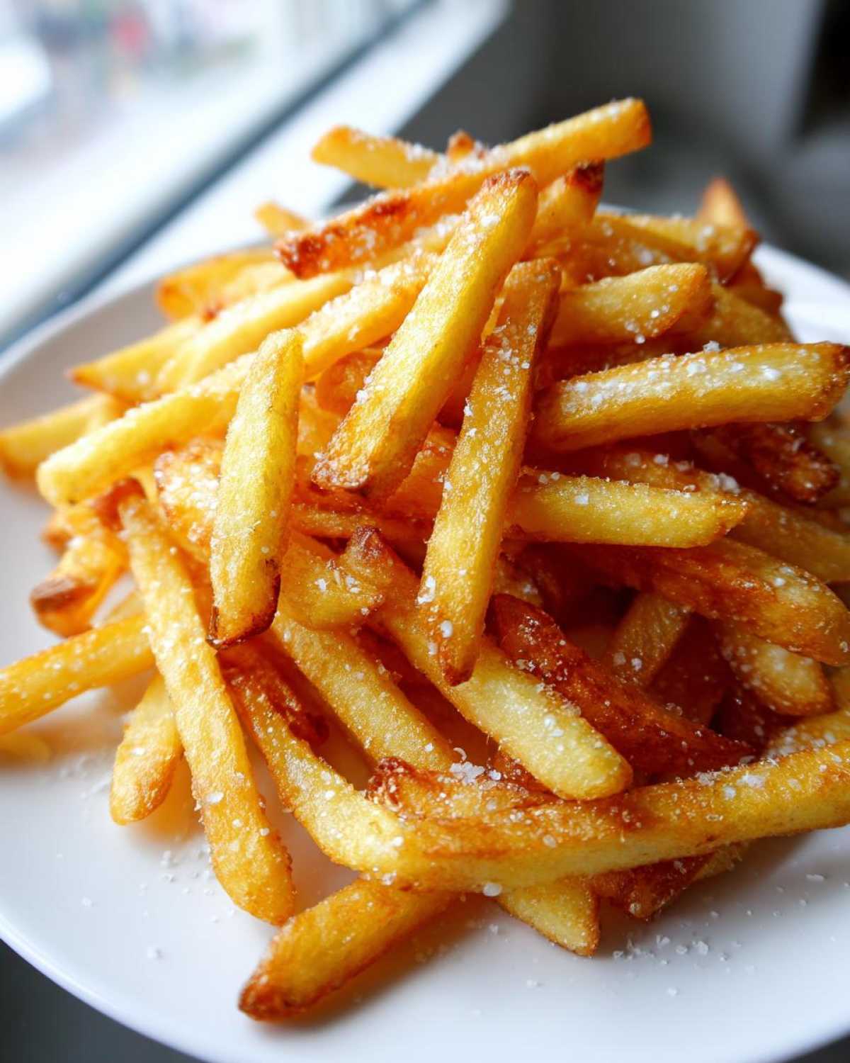 Close-up of a pile of golden, crispy air fryer french fries sprinkled generously with coarse salt.