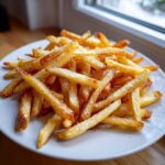 A close-up of golden, crispy air fryer french fries dusted with seasoning on a white plate.