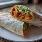 A crispy buffalo chicken wrap cut in half, showing spicy chicken, lettuce, and ranch dressing inside a flour tortilla.