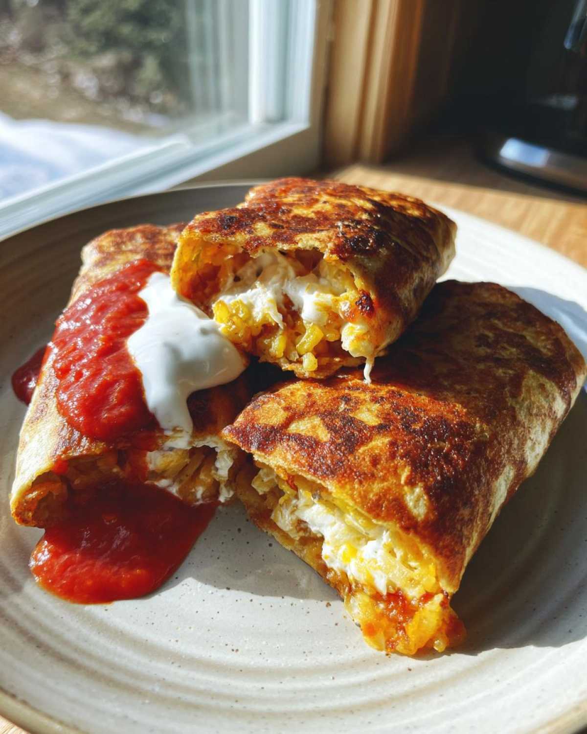 Two crispy, pan-fried potato tacos cut open to show the filling, topped with red salsa and sour cream.