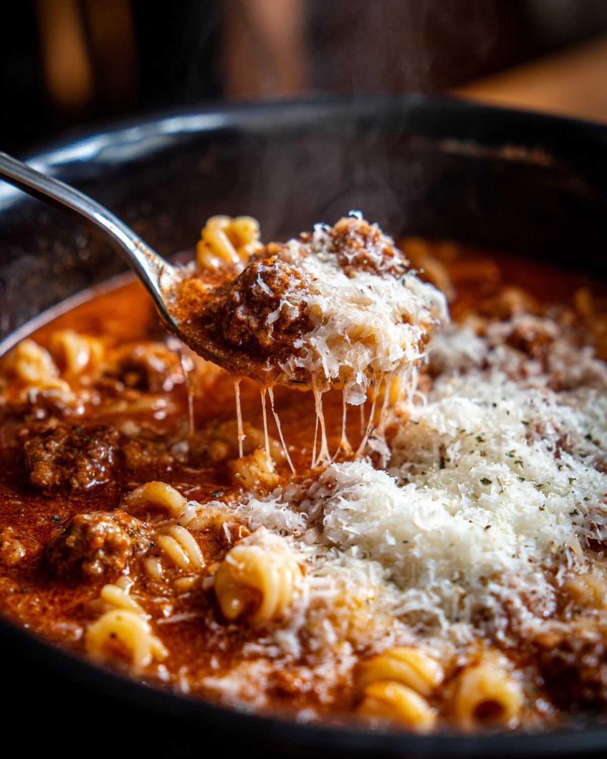A spoonful of hot crockpot lasagna soup showing a cheesy meatball and pasta being lifted from the rich tomato broth.