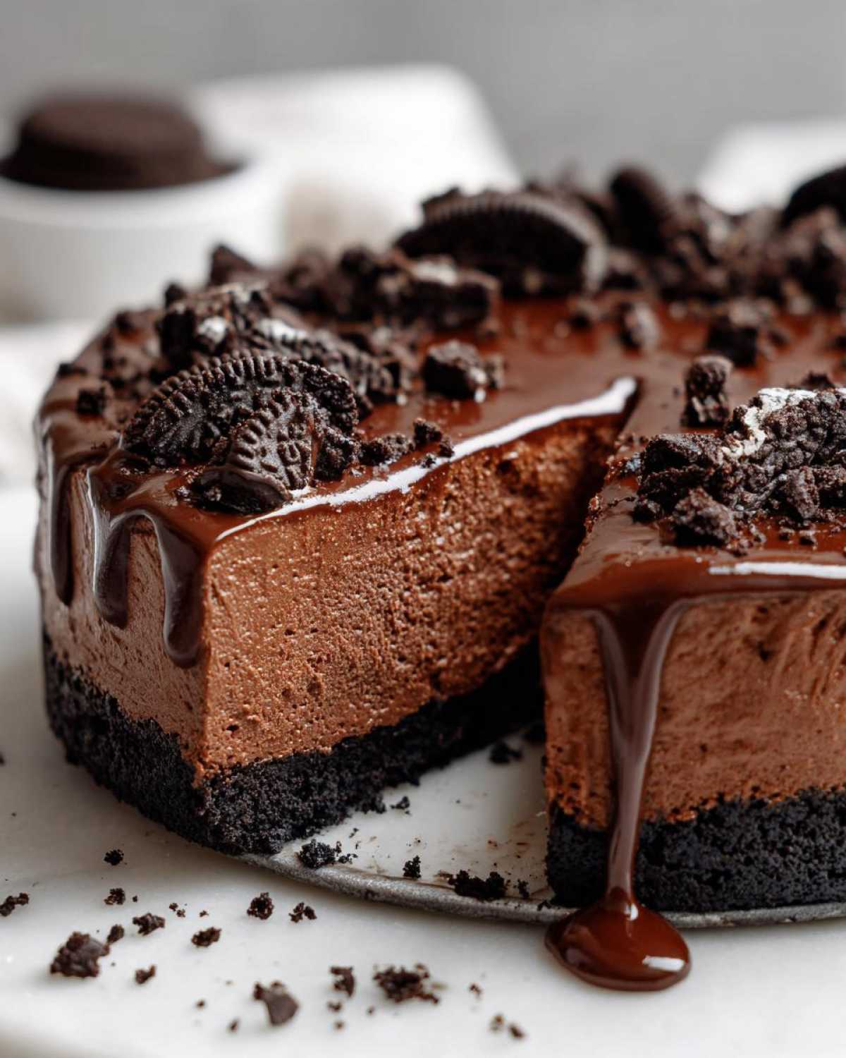 A slice removed from a rich chocolate mousse pie with an Oreo crust, topped with ganache and cookie crumbles.