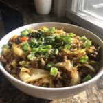 A close-up of a white bowl filled with savory Egg Roll in a Bowl, topped generously with sliced green onions and sesame seeds.