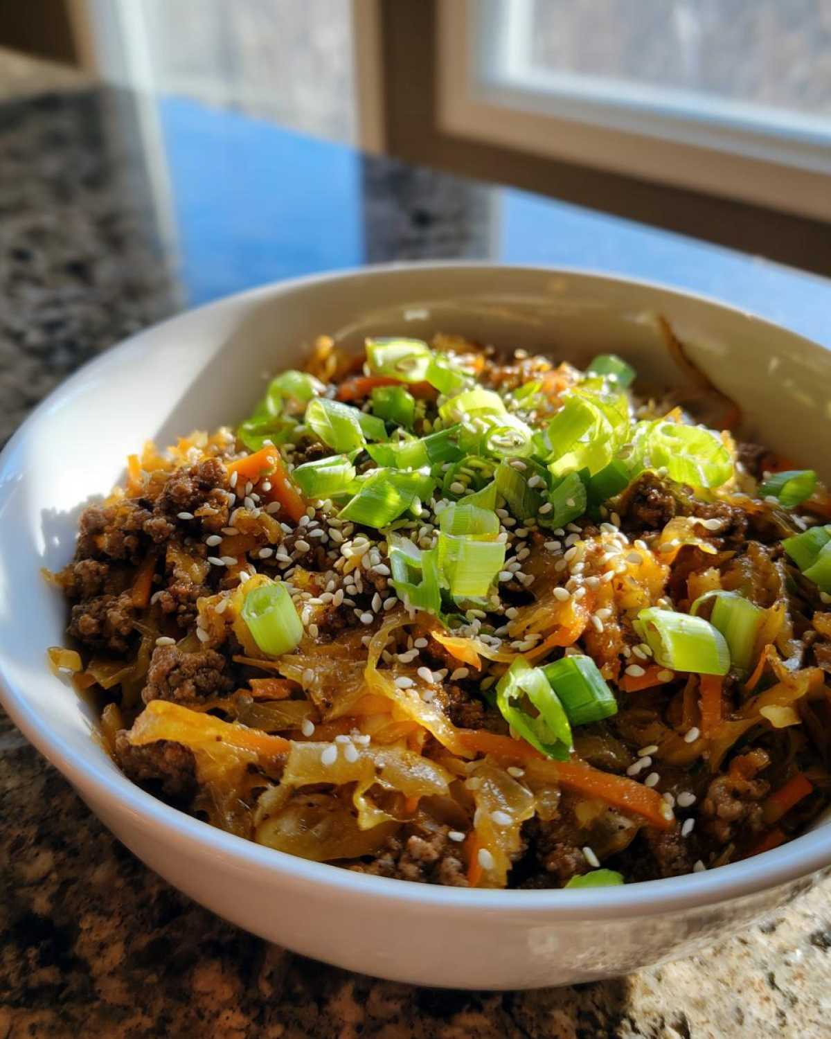 A white bowl filled with savory Egg Roll in a Bowl mixture, topped with sesame seeds and fresh green onions.