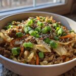 A close-up of a white bowl filled with Egg Roll in a Bowl, topped with sesame seeds and fresh green onions.