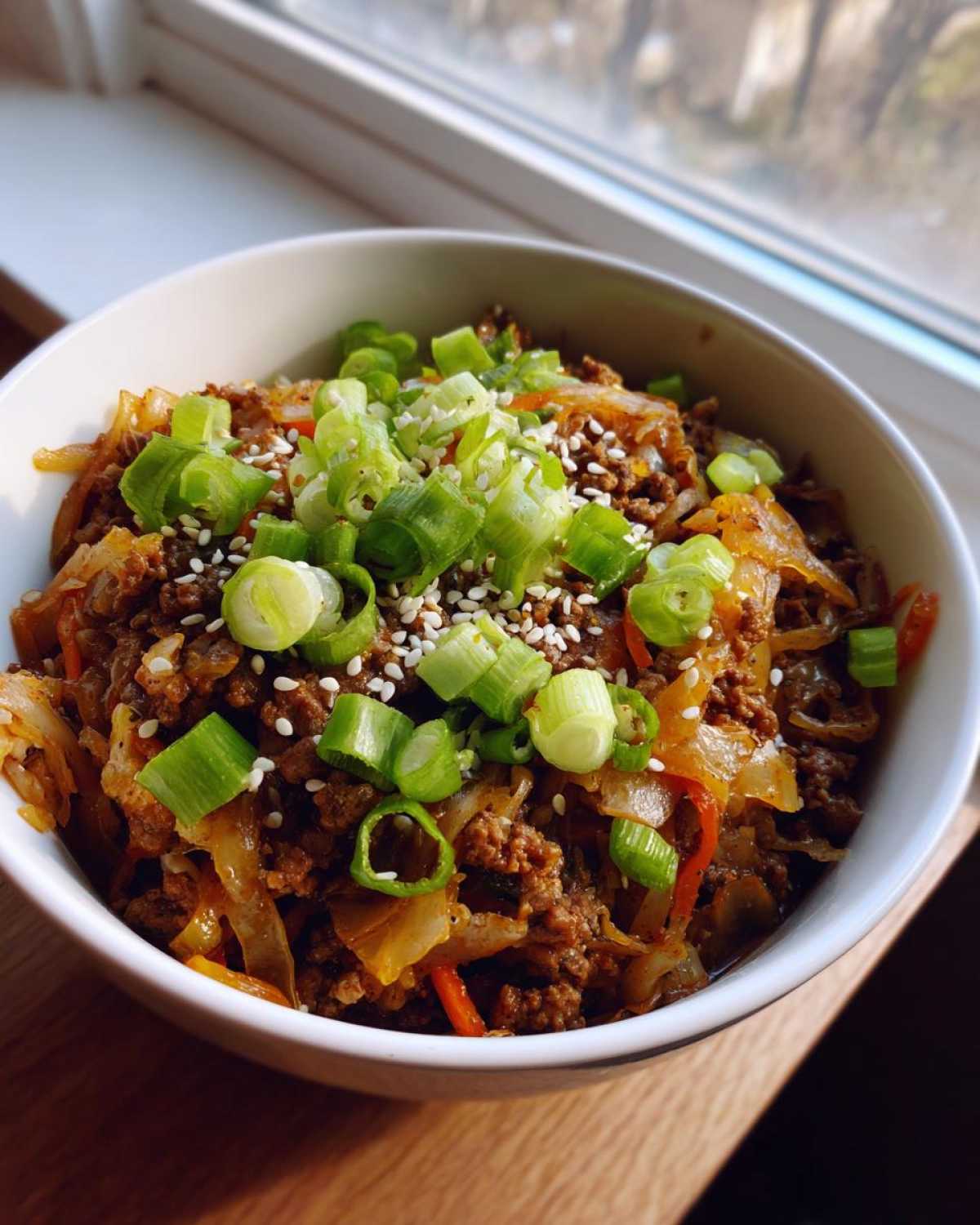 Close-up of a white bowl filled with savory Egg Roll in a Bowl mixture, topped with fresh green onions and sesame seeds.