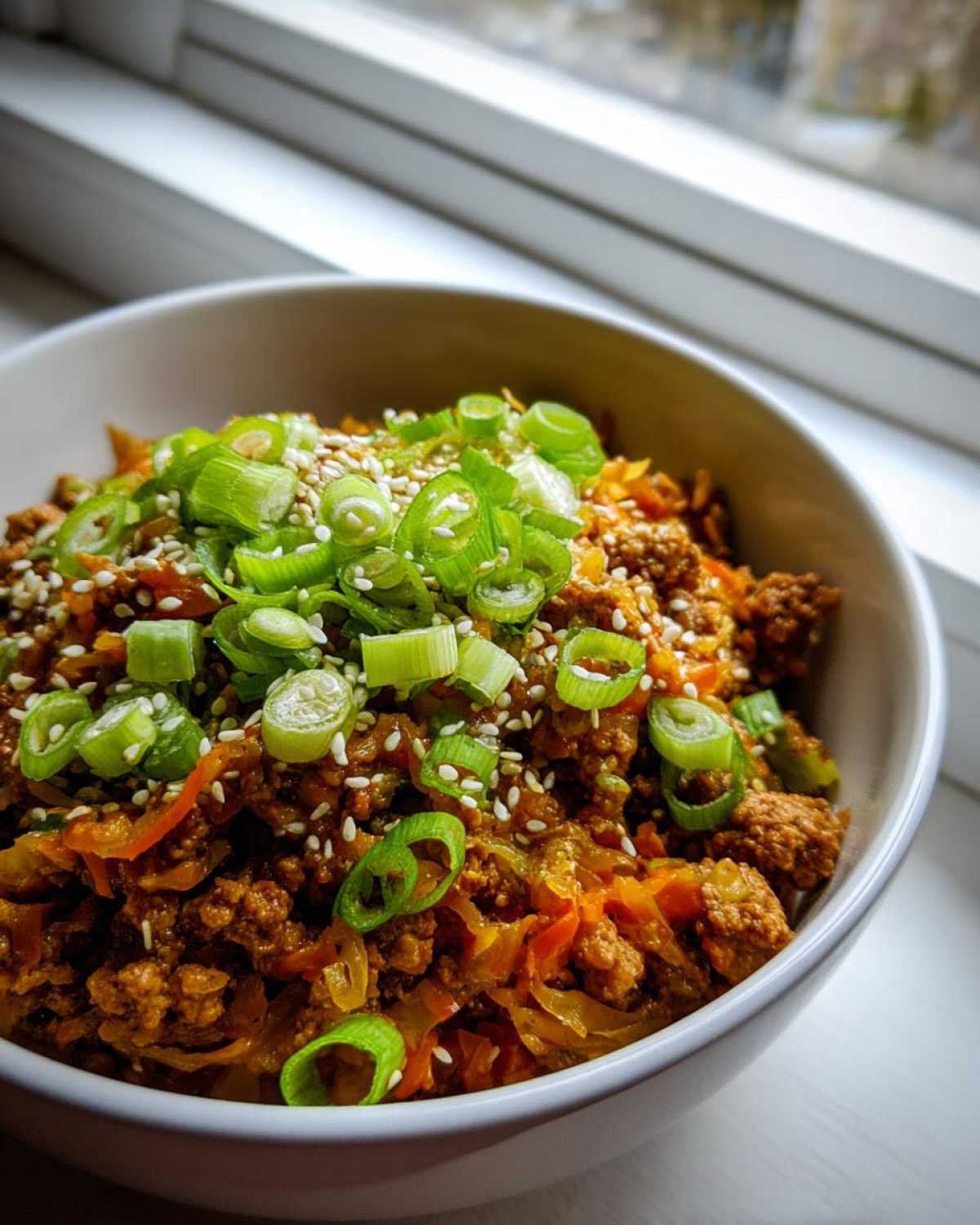 Close-up of a serving of Egg Roll in a Bowl, featuring ground meat, cabbage, topped with green onions and sesame seeds.
